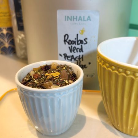 El Rooibos verde con melocotón "Peach Melba" es novedad para este verano, prepáralo "en frío", te encantará. Sus ingredientes son trocitos de melocotón, papaya, hibiscus y pétalos de girasol. El Rooibos (Aspalthus Linearis) no contiene cafeína por tanto lo podemos tomar tranquilamente por la tarde y después de cenar en caso de personas sensibles a la cafeína. El Rooibos verde es el mismo que el Rooibos que ya conocemos habitualmente pero conserva el color verde natural en sus hojas ya que una vez hecha la cosecha se para la oxidación por un proceso de calor, obteniendo así una bebida más fresca en sabor y más rica en antioxidantes. El Rooibos es apto para todas las personas: niños, adultos, personas mayores. Contiene muchos antioxidantes, vitaminas y minerales beneficiosos para nuestro organismo. En nuestra tienda podrás disfrutar de una amplia selección de Rooibos que siempre podrá ir acompañado de unas buenas galletas. En INHALA Cafés y Tés encontrarás cafés recién tostados, tés e infusiones, chocolates selectos y deliciosas galletas. Estamos en Portalet, 9 de Granollers, Barcelona.